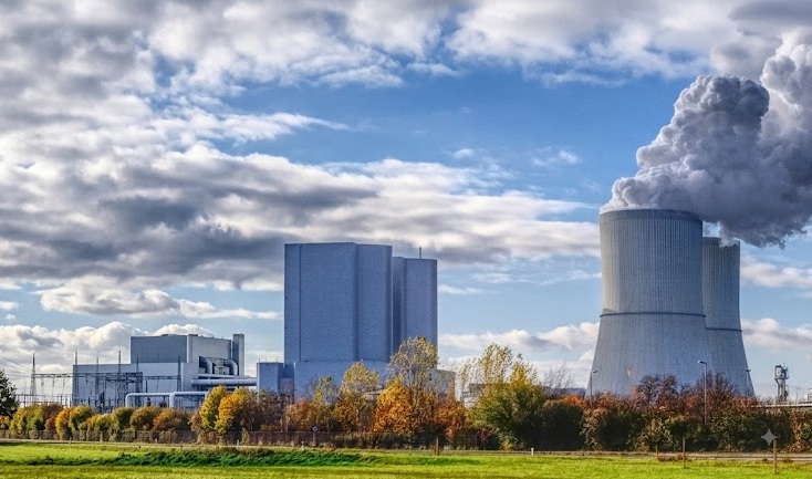 Power plant cooling towers with steam behind an autumn treeline